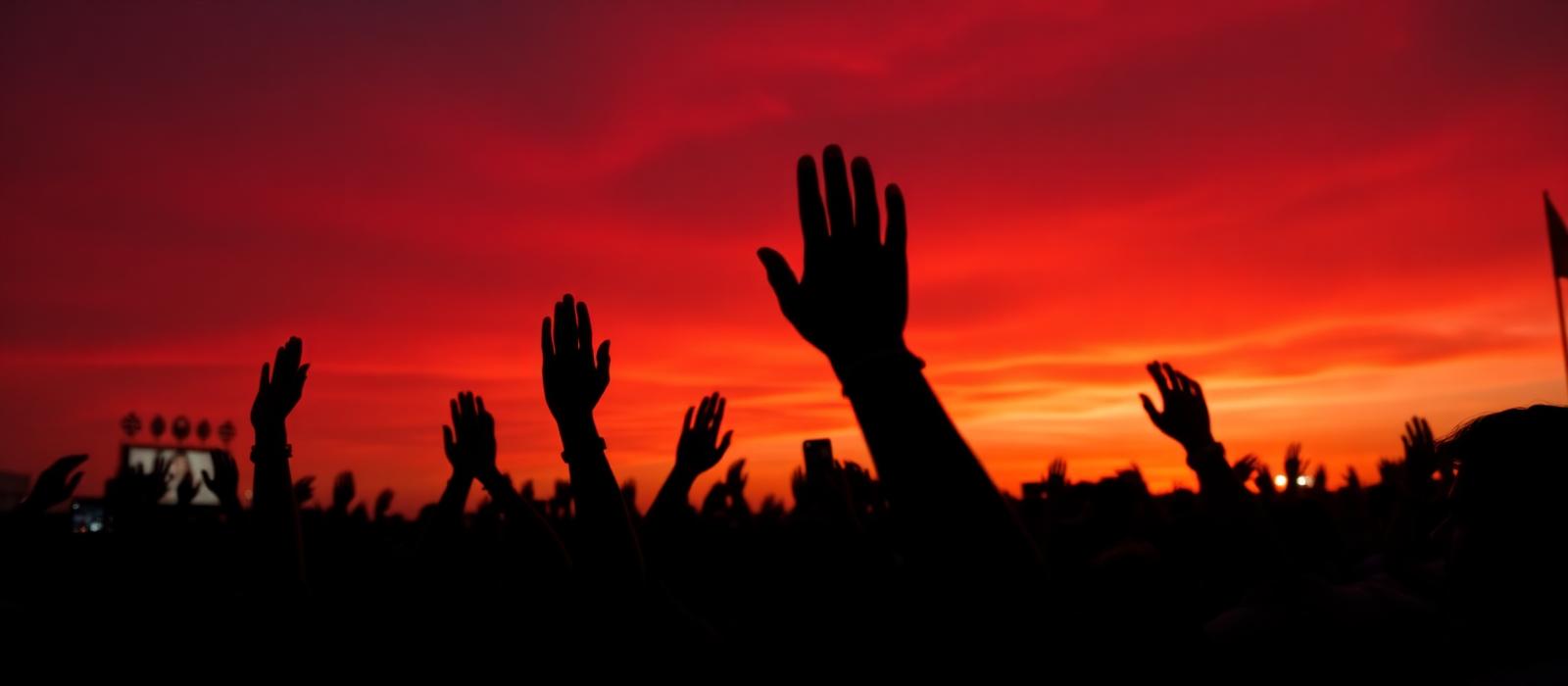 Crowd of young supporters raising their hands at a national rally at sunset